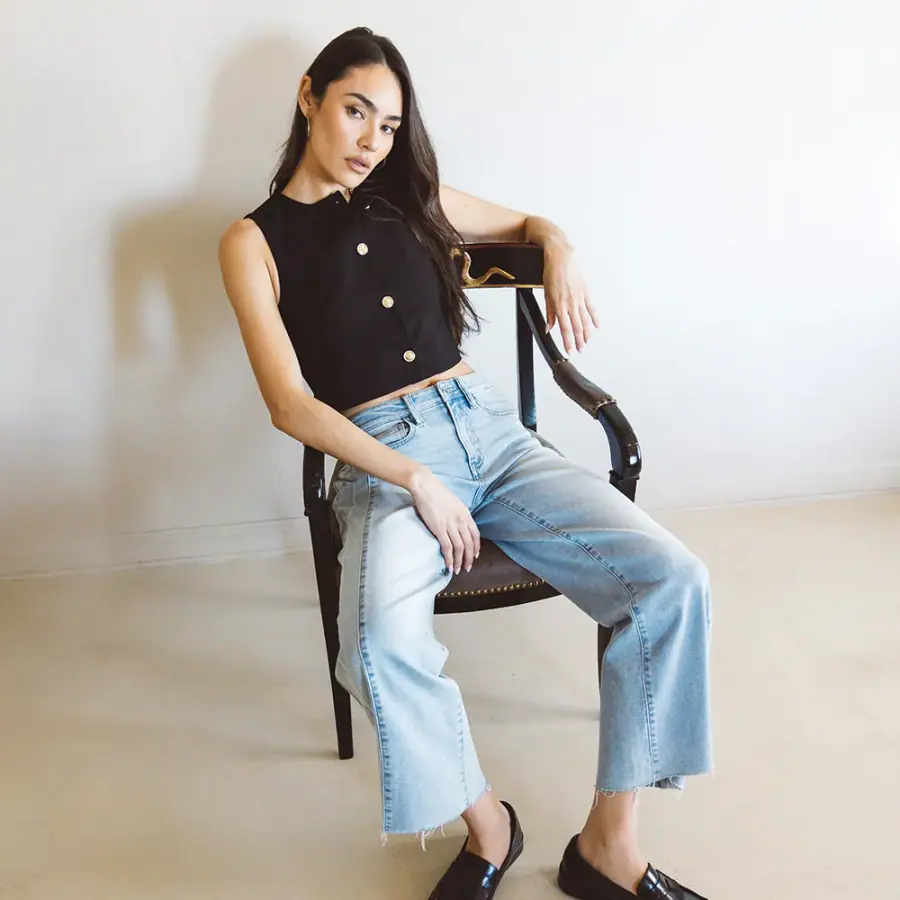 Woman seated in a chair wearing light-blue wide-leg jeans and a black sleeveless buttoned top.