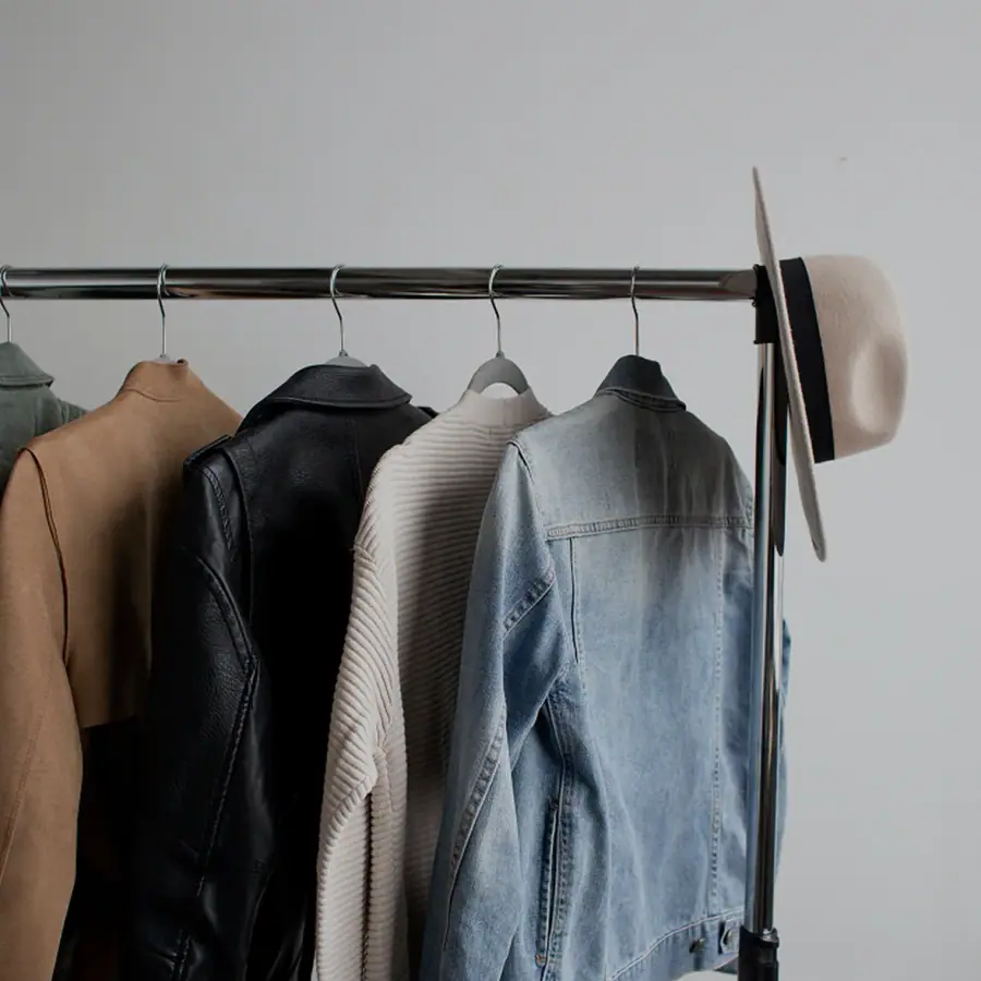 Denim jacket and neutral-toned clothing hanging on a black garment rail.